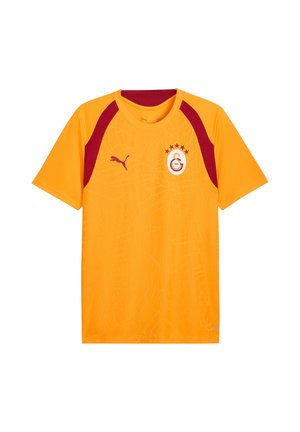 Maglia sportiva arancione a maniche corte con accenti rosso scuro, logo Puma sul petto destro e stemma del club di calcio Galatasaray sul petto sinistro.