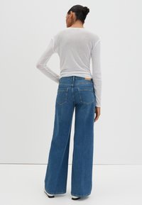 Jean en denim bleu à jambe large avec une taille mi-haute et un design à cinq poches. Le matériau est doux avec une texture lisse et des détails de couture minimaux.
