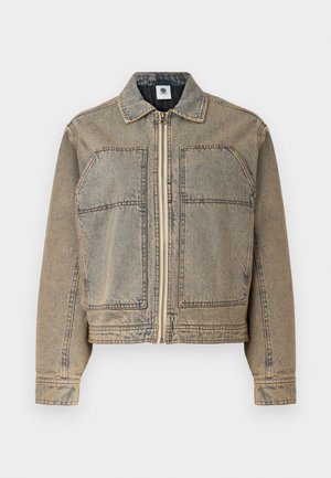 Lys brun denimjakke med glidelås, to brystlommer og en strukturert silhuett med kontrasterende sømmer.