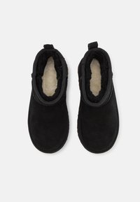 Botas de tobillo de ante negro con forro de felpa suave, punta redondeada y lengüeta en la parte posterior para facilitar el uso. Suela de goma plana.