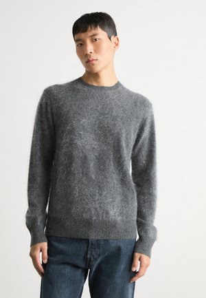 Maglione grigio lavorato a maglia con texture pelosa, scollo a girocollo e polsini e orlo a costine, abbinato a jeans scuri in denim.