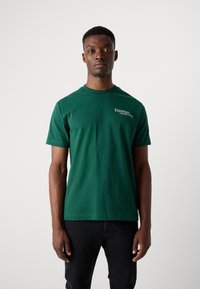 Green cotton t-shirt with short sleeves and a crew neck, featuring white text "Espresso Awakening" on the front, smooth texture.