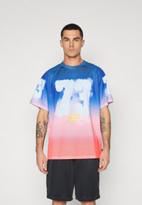 T-shirt en mesh à manches courtes dégradé bleu à rose, avec un motif de nuages et un texte jaune. Porté avec un short noir, doté d'un col rond.