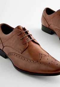 Chaussures habillées en cuir marron avec un bout pointu, des détails en ailes et des accents en tissu texturé. Présentant un système de laçage et une semelle noire.