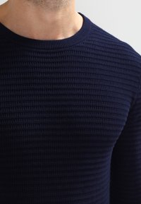 Námořnický modrý pletený svetr s texturovaným, žebrovaným vzorem a kulatým výstřihem. Měkká látka střední tloušťky vhodná pro vrstvení.