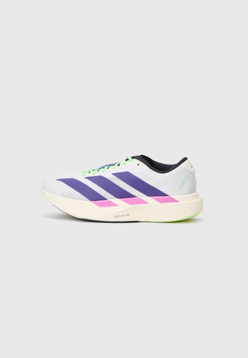 Chaussure de course blanche avec des bandes violettes, des touches roses, des lacets vert néon et une semelle épaisse crème sur un fond gris uni.