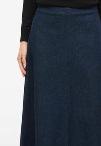Długa spódnica dżinsowa w ciemnym odcieniu niebieskiego, o gładkiej fakturze, z wysokim stanem i prostym krojem. Posiada środkowy szew, bez widocznych ozdób.