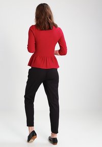 Haut peplum rouge à rayures avec des manches longues, associé à un pantalon noir ajusté et des chaussures noires avec un talon marron, pris de dos.