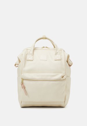 Beige batoh se strukturovaným tvarem, vyrobený z hladké látky. Disponuje dvojicí uší, přední kapsou na zip a zlatými kovovými detaily.