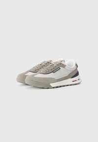 Grey suede and textile sneakers with a white midsole, padded tongue, and navy accent at the rear; chunky sole with red and blue detail.