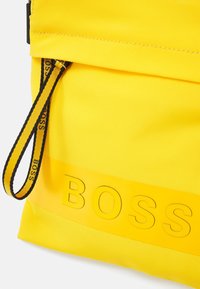 Pouch di tessuto giallo con una cerniera nera e gialla con marchio, caratterizzato da testo in rilievo "BOSS" nella parte inferiore.