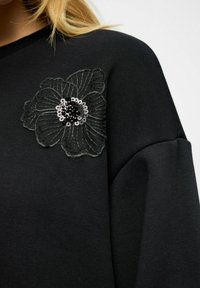 Sudadera negra con un aplique de flor bordado con lentejuelas, costuras texturizadas y un escote redondeado. Acabado de tejido suave.