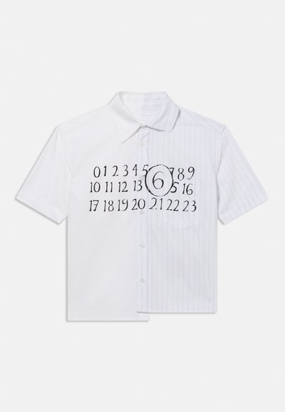 Πουκάμισο με κοντά μανίκια και κουμπιά, με το μισό σε μονόχρωμο λευκό και το άλλο μισό λευκό με μπλε ρίγες, και μαύροι αριθμοί 0-23 τυπωμένοι, με τον αριθμό 6 κυκλωμένο στο κέντρο μπροστά.