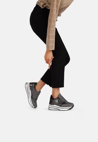 Sneaker grigia con una finitura testurizzata e lucida, dotata di una suola bianca spessa, con un design a laccio e accenti neri discreti.