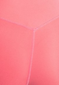 Rosa sportleggings med en slät textur. Synliga sömmar och en kontrasterande sömdetalj förstärker den övergripande strukturen.