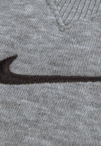 Γκρι πλεκτό πουλόβερ με λαιμόκοψη σε σχήμα V, με έντονο σκούρο καφέ λογότυπο Nike swoosh κεντημένο στο μπροστινό μέρος.