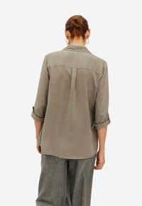 Grijze, lichte knoopshirt met opgerolde mouwen en een rugplooitje. Zachte textuur, rechte snit en een eenvoudig ontwerp.