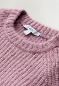 Hellrosa gestrickter Pullover mit einer gerippten Textur, einem weiten Ausschnitt und einem Etikett mit der Aufschrift "NEXT" am Kragen.