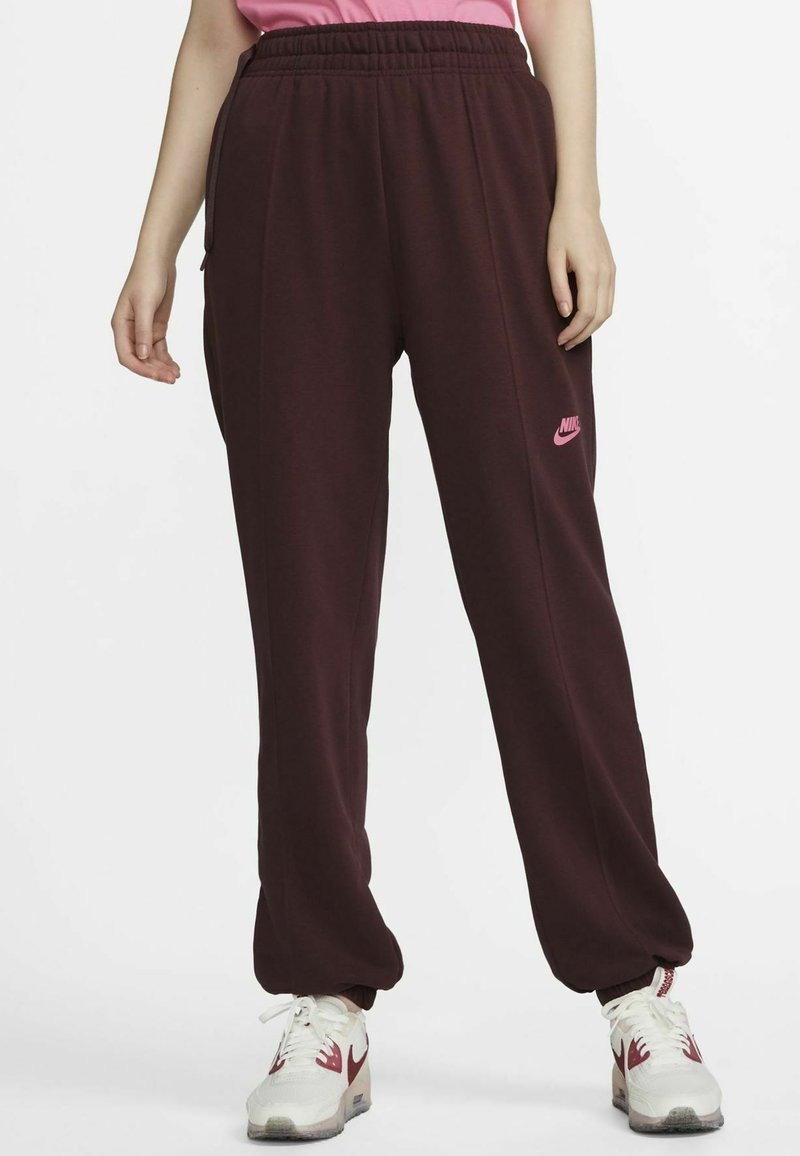 Burgundy sweatpants with an elastic waistband, side pockets, and a pink Nike logo on the left thigh. Soft, textured material.