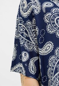 Mörkblå tyg med vita paisley- och blommönster. Kortärmad design, slät textur med intrikata detaljer och accenter.