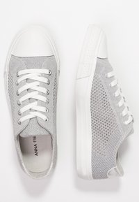 Harmaat verkkomaiset lenkkarit valkoisilla kumipohjilla, joissa on litteät valkoiset nauhat, ommeltuja yksityiskohtia ja teksturoitu sivupaneeli.