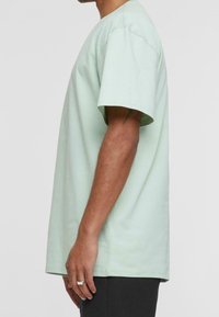 Miętowa bawełniana koszulka z krótkim rękawem, luźny krój i okrągły dekolt, o gładkiej teksturze i minimalistycznych detalach.