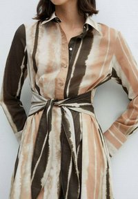 Lange mouwende jurk in beige, bruin en roomkleurige strepen, met een kraag en een strikdetail in de taille. Glad materiaal met een subtiele glans.