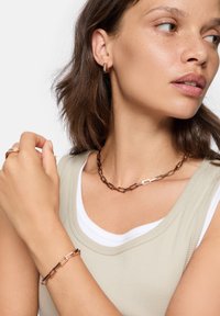 Smykkesæt i rosaguld bestående af en sammenkoblet halskæde og matchende armbånd med rektangulære detaljer. Glat tekstur, moderne design.