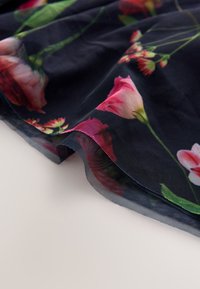 Transparenter, dunkler Stoff mit bunten Blumenmustern, darunter rosa und grüne Farbtöne, mit fließender Textur und geschwungenen Kanten.