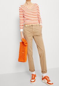 Rood-wit gestreepte lange mouwen top; beige broek; oranje gebreide tas; witte sneakers met oranje accenten; casual ensemble; opgerolde broekspijpen.