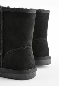 Schwarze Wildleder-Ankle-Boots mit einem weichen fellbesatz, ausgestattet mit einer strukturierten Gummisohle und genähten Details entlang der Nähte.