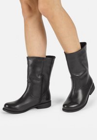 Botines de cuero negro hasta el tobillo con punta redonda, cremallera lateral y un tacón bajo texturizado. Acabado suave con un ligero brillo.