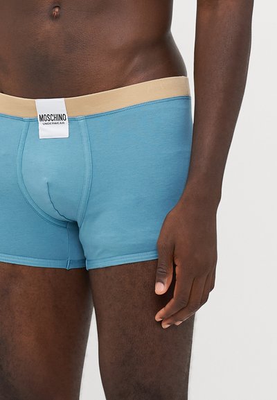 Blue cotton boxer briefs with a beige elastic waistband featuring a logo label. The fabric is smooth with a snug fit.