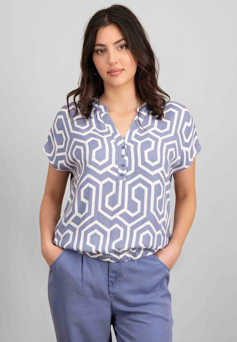Blusa a maniche corte di colore azzurro chiaro con motivo geometrico bianco, caratterizzata da un colletto e dettagli con bottoni. Tessuto morbido con vestibilità rilassata.