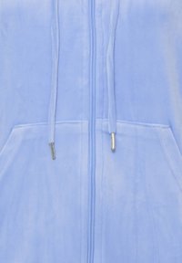 Sweat à capuche bleu clair à fermeture éclair en tissu doux et texturé. Comprend deux poches avant, une capuche avec cordon de serrage et des accents de quincaillerie argentée.