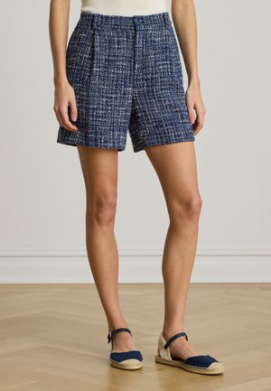 Krátke nohavice z tvídu v námorníckej modrej farbe s bielymi škvrnkami, s vysokým pásom, záhybmi a voľným strihom. Kombinované s námorníckymi espadrilkami.