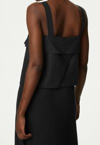 Débardeur noir à couches avec des bretelles larges et un design fluide. Fabriqué en tissu léger, avec un détail dans le dos composé d'une couture horizontale.