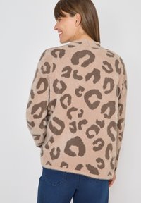 Leopardmönstrad kofta i mjuk beige tyg, med mörkbruna abstrakta fläckar, avslappnad passform och ribbad halsringning. Avslappnad och komfortabel design.