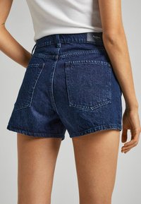 Denim shorts in dark blue with a high waist. Features include double back pockets, belt loops, and a rolled hem. Textured fabric.
