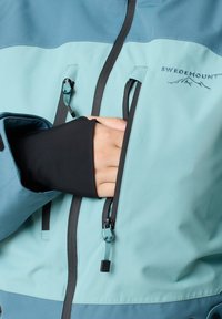 Teal and light blue waterproof jacket with black accents, featuring a front zipper, pocket openings, and a fitted cuff. SWEDEMOUNT logo displayed.