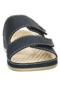 Sandale noire avec deux brides en velcro, semelle intérieure texturée, orteils arrondis et semelle beige contrastante. Détails cousus le long des bords.