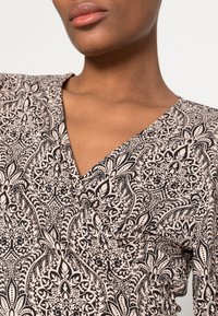 Top envolvente negro con crema, con un diseño de escote en V, que presenta intrincados motivos florales y de paisley. Tejido suave y ligero.