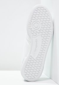 Suola di sneaker bianca in gomma con motivo strutturato e tallone arrotondato. Presenta nome del marchio in rilievo e design del logo circolare.