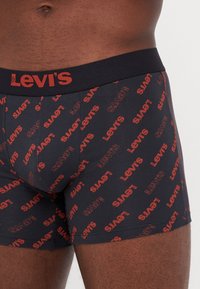 Svarta boxerkalsonger med röd "Levi's"-logotyp och upprepande textmönster, med ett mjukt elastiskt midjeband för komfort.