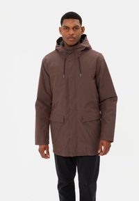 Giubbotto impermeabile marrone con cappuccio, cordino regolabile e due tasche frontali. Tessuto liscio, design di lunghezza media adatto a diverse condizioni atmosferiche.
