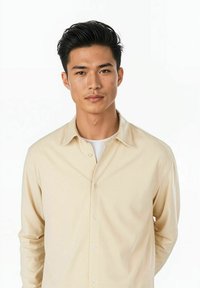 Beige långärmad skjorta med knäppning fram, nedvikt krage och slät textur, över en vit skjorta, visad på en modell.