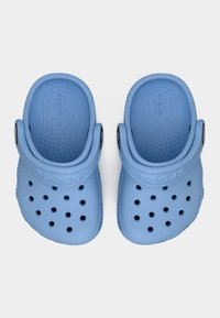 Ζευγάρι ανοιχτόχρωμων γαλάζιων πάντων με τρύπες αερισμού και ρυθμιζόμενα λουριά στο πίσω μέρος, εμφανιζόμενα από πάνω σε λευκό φόντο.