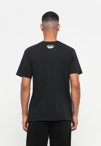 Juoda medvilninė palaidinė su apvalia iškirpte ir trumpomis rankovėmis. Ant viršutinės nugaros dalies yra baltas logotipas, o apačia tiesi.