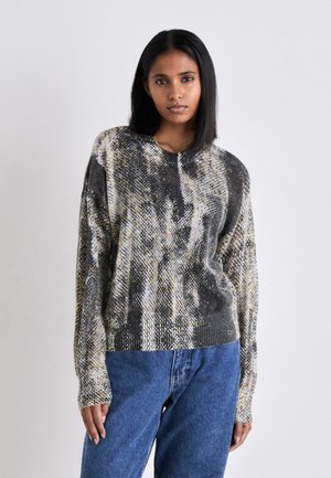 Pull en maille avec un motif texturé dans des tons de gris, noir et jaune. Encolure ronde et manches longues. Associé à un jean bleu taille haute.