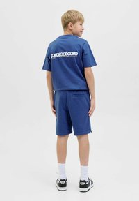 Blå bomulls t-shirt med logga på ryggen och matchande shorts. Outfiten har en avslappnad passform, korta ärmar och sidofickor. Svarta sneakers.
